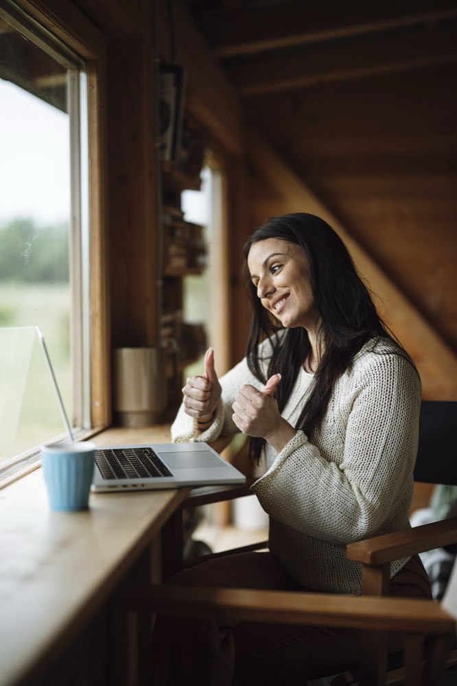 Woman at a wooden desk giving a thumbs up to her laptop